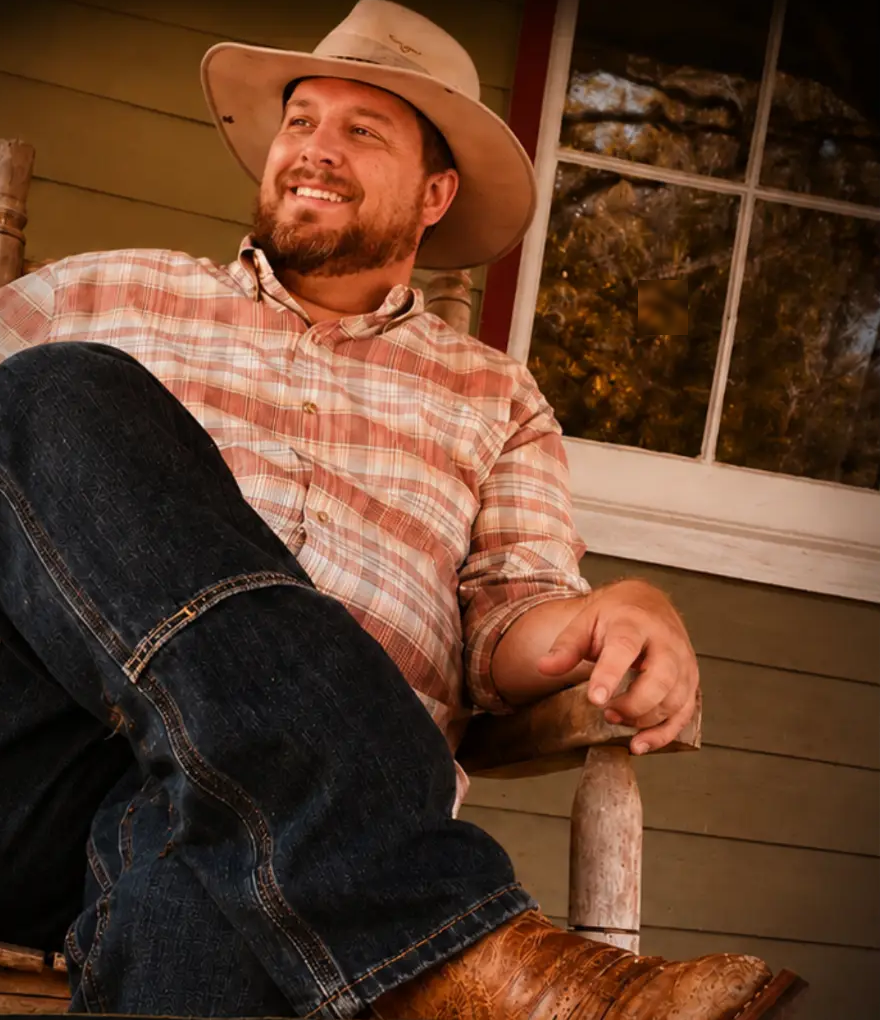 Raymond Alston smiling in a cowboy hat on a ranch porch